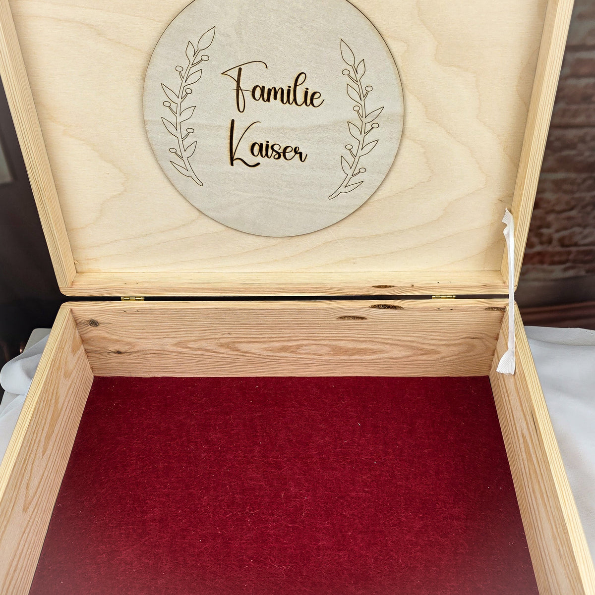 Personalisierte Erinnerungsbox aus Holz geöffnet – Innenansicht mit roter Filzeinlage und graviertem Holzanhänger „Familie Kaiser" von Wunschhandwerk